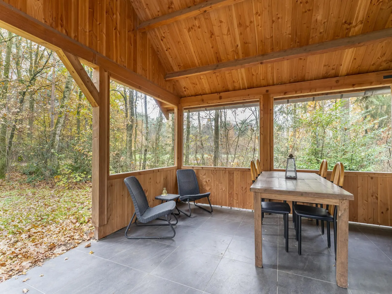 Under the timber veranda roof: dining table and two lounge chairs, looking into the woods