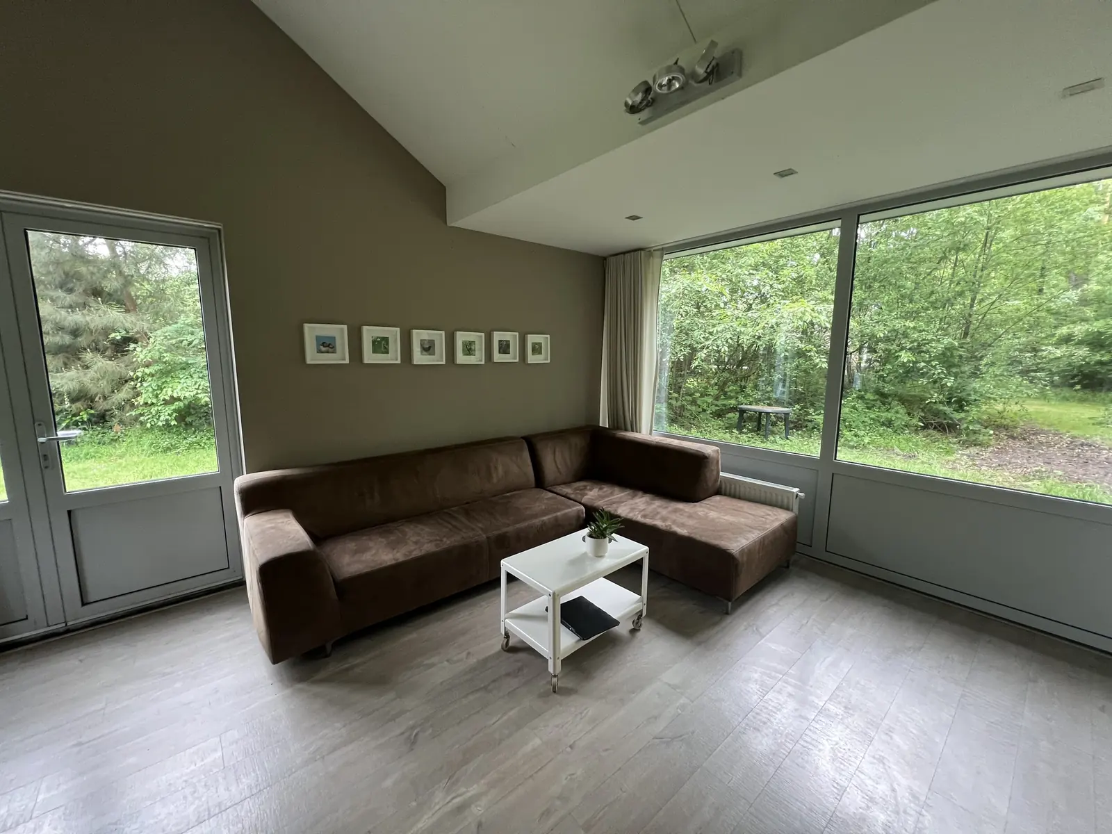 Brown corner sofa, a glass door to the outside and windows looking out on the trees