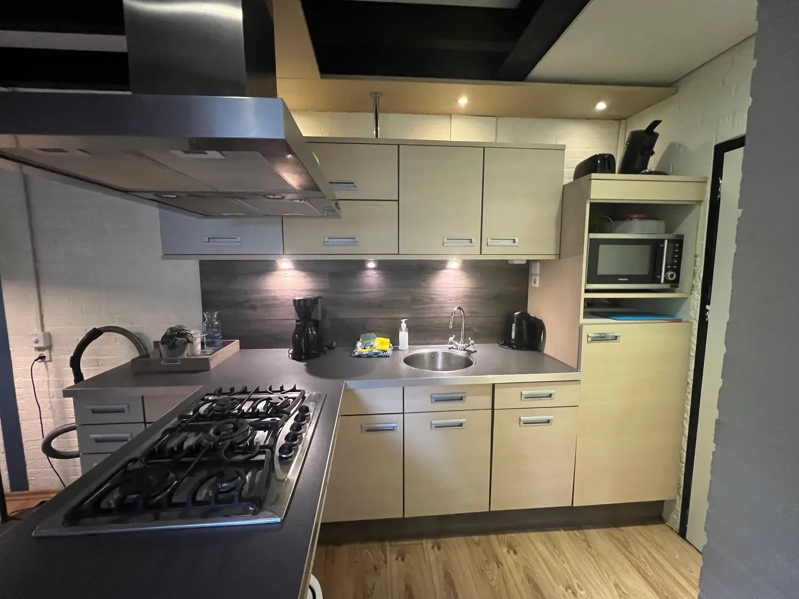 Kitchen with a gas hob under a large extractor hood, a microwave and a coffee maker