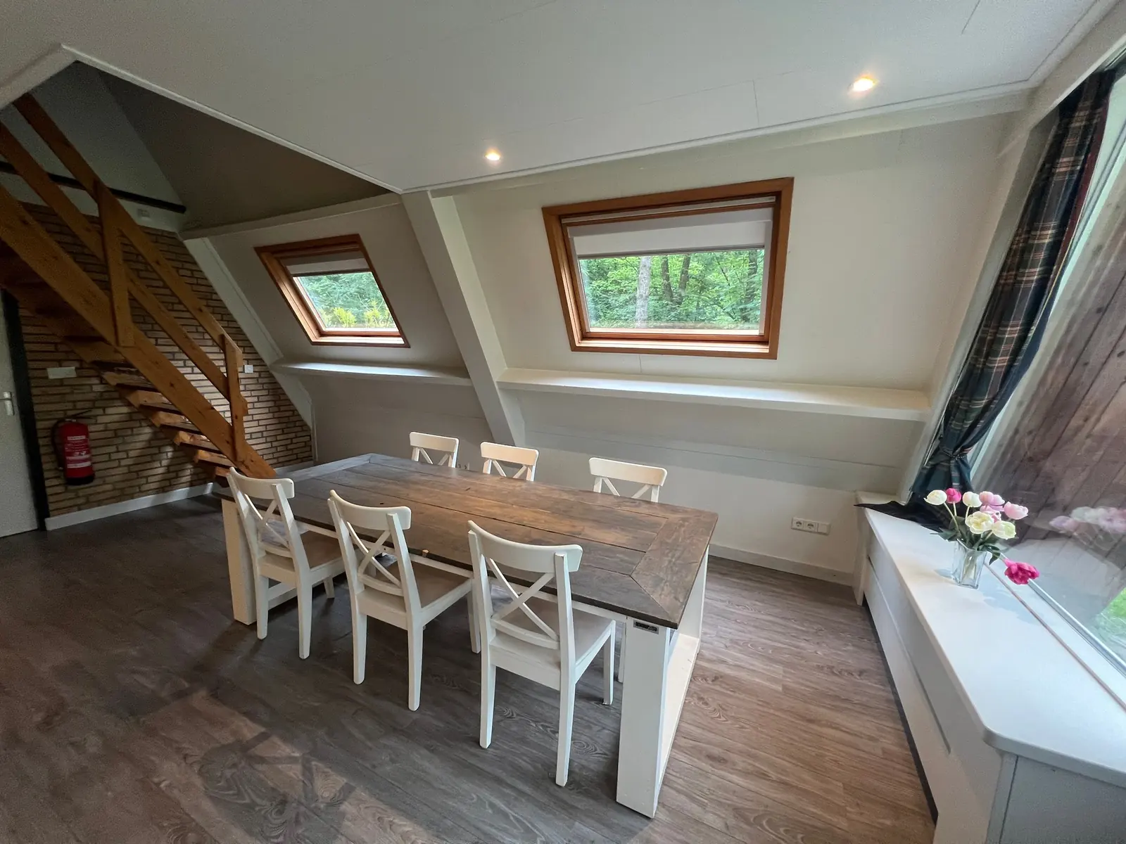 Wooden dining table with six white chairs under two roof windows