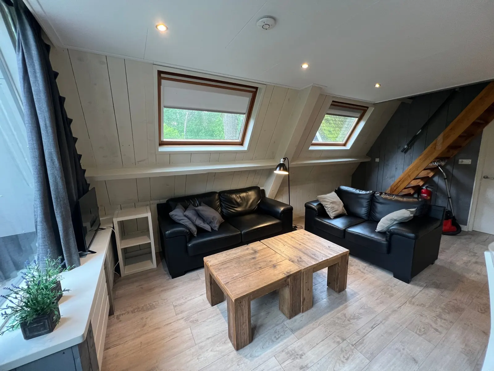 Seating area with two black leather sofas and two wooden coffee tables under two roof windows
