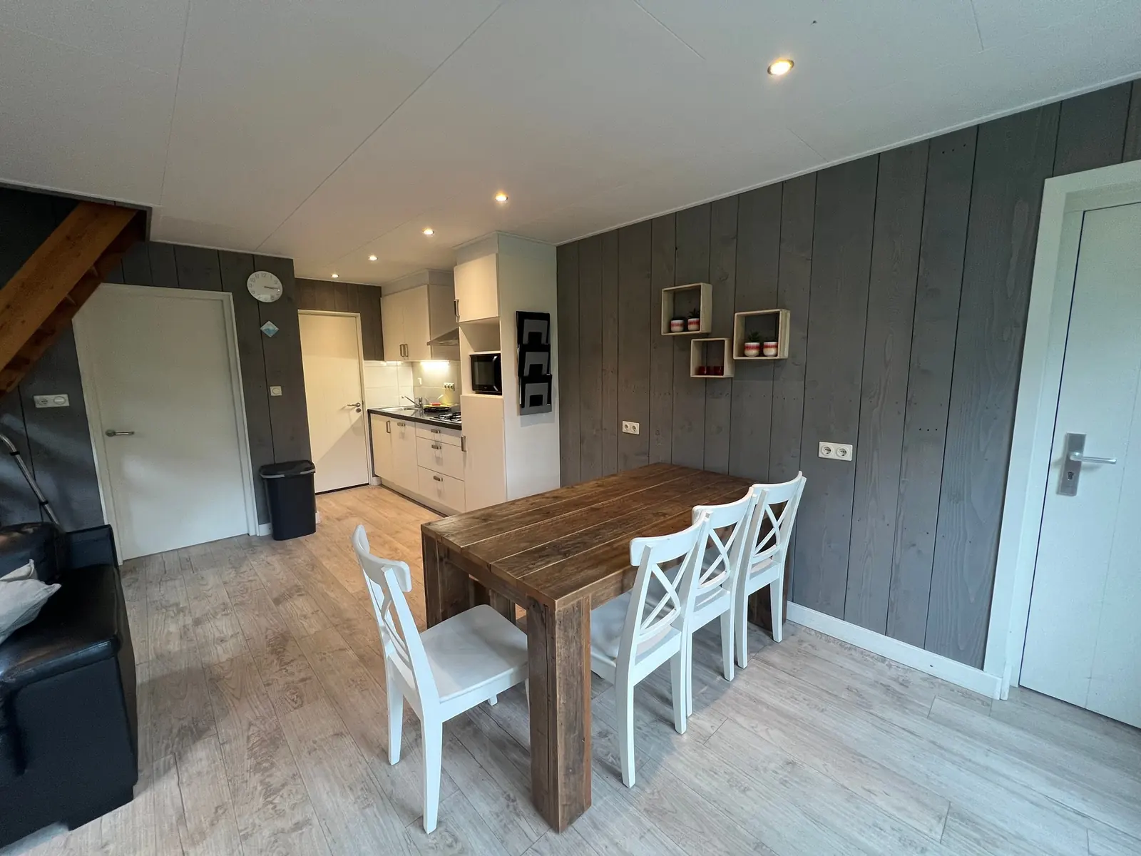 Wooden dining table with white chairs, the kitchen behind
