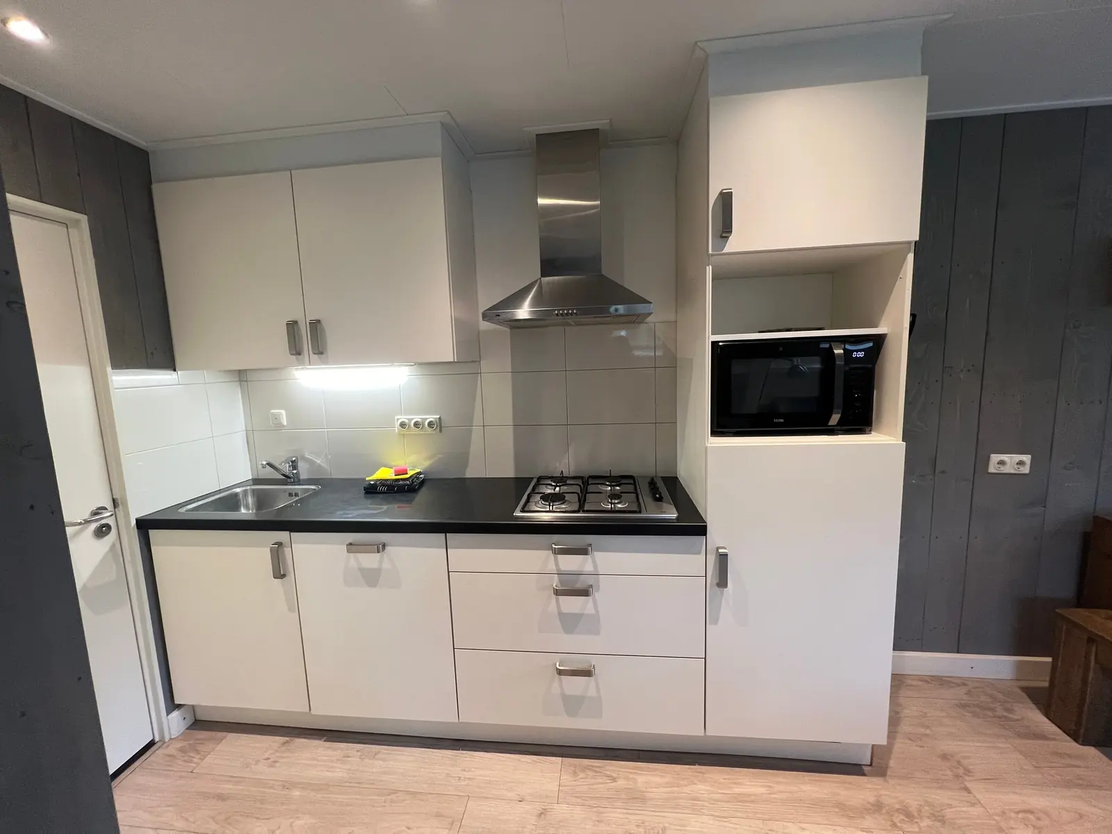 Kitchen with white units, gas hob, extractor hood and microwave