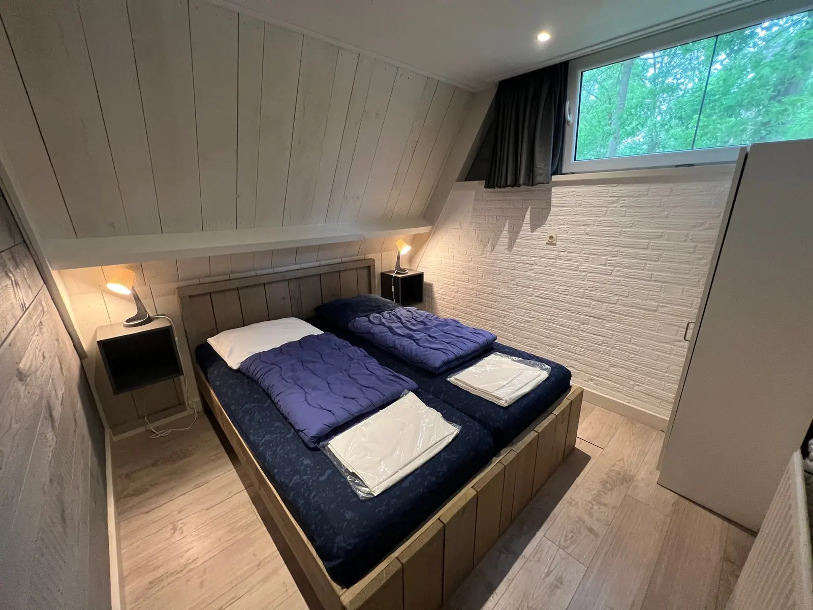 Bedroom with a wooden double bed and a white brick wall