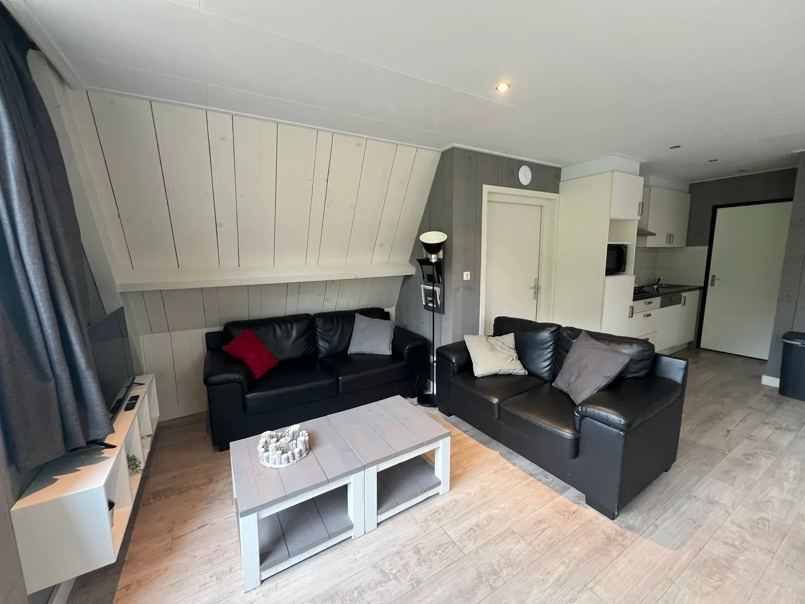 Seating area with two black leather sofas, coffee tables and TV, the kitchen behind
