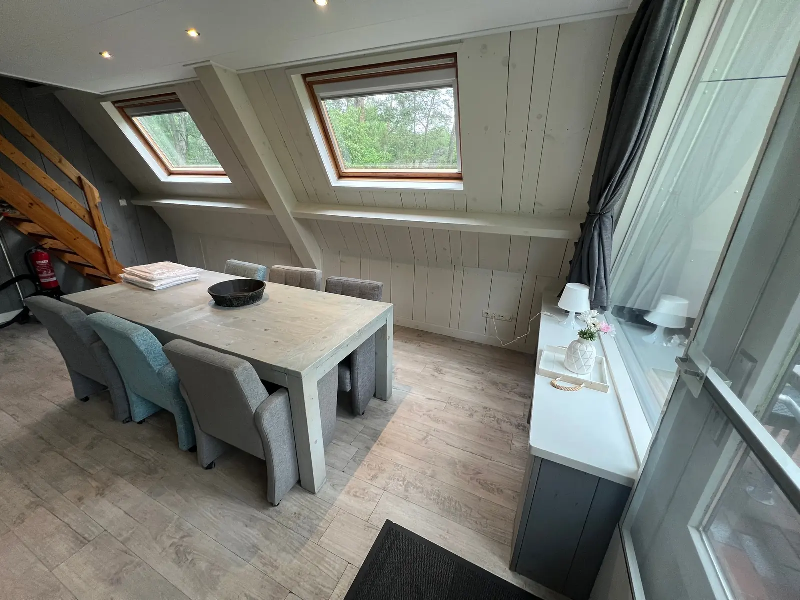 Dining table with grey upholstered chairs under two roof windows