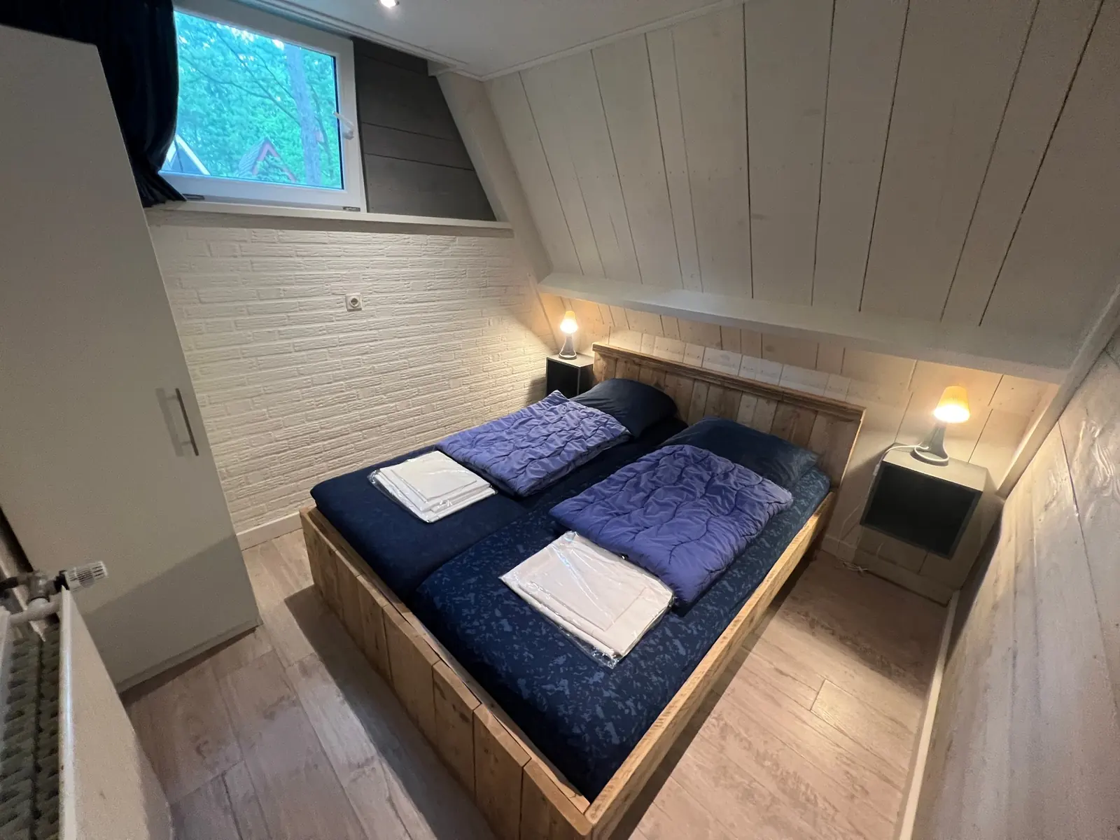Bedroom with a wooden double bed and a white brick wall