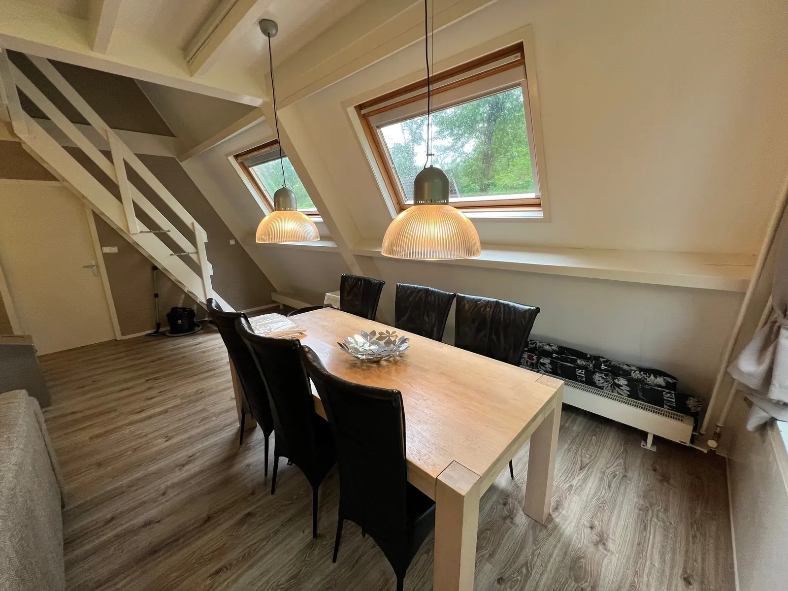 Dining table with six black chairs under two roof windows and pendant lamps